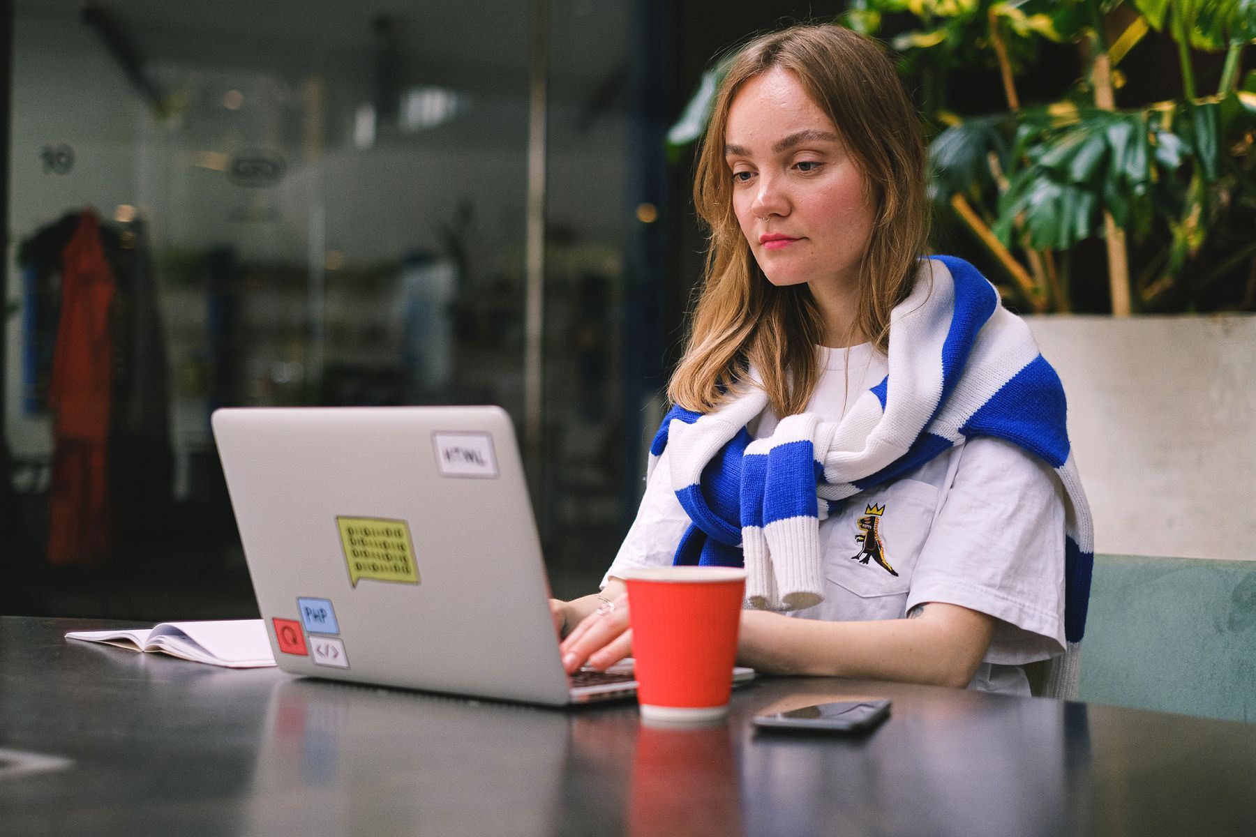 Młoda osoba pracująca na laptopie przy stoliku w kawiarni