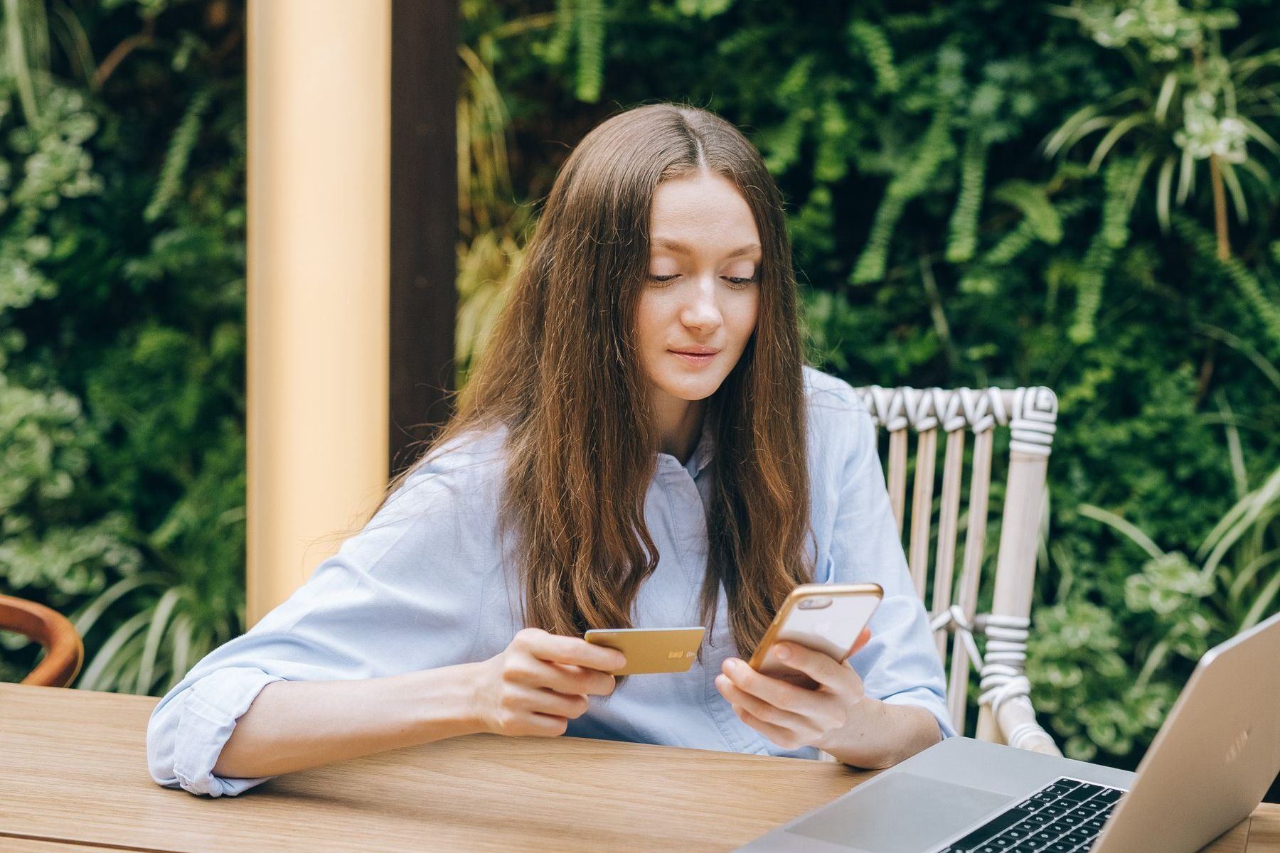 Kobieta trzymająca kartę płatniczą i smartfon przy laptopie